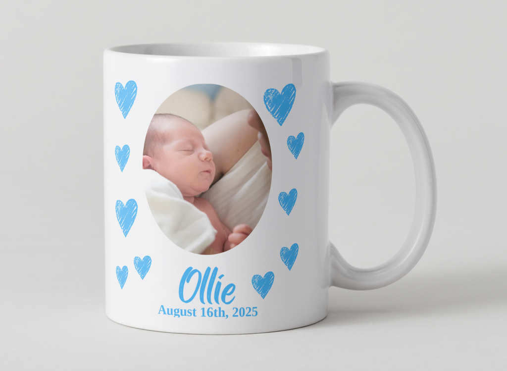 White mug with a photo of a baby and blue hearts, featuring the name 'Ollie' and date 'August 16th, 2025'.