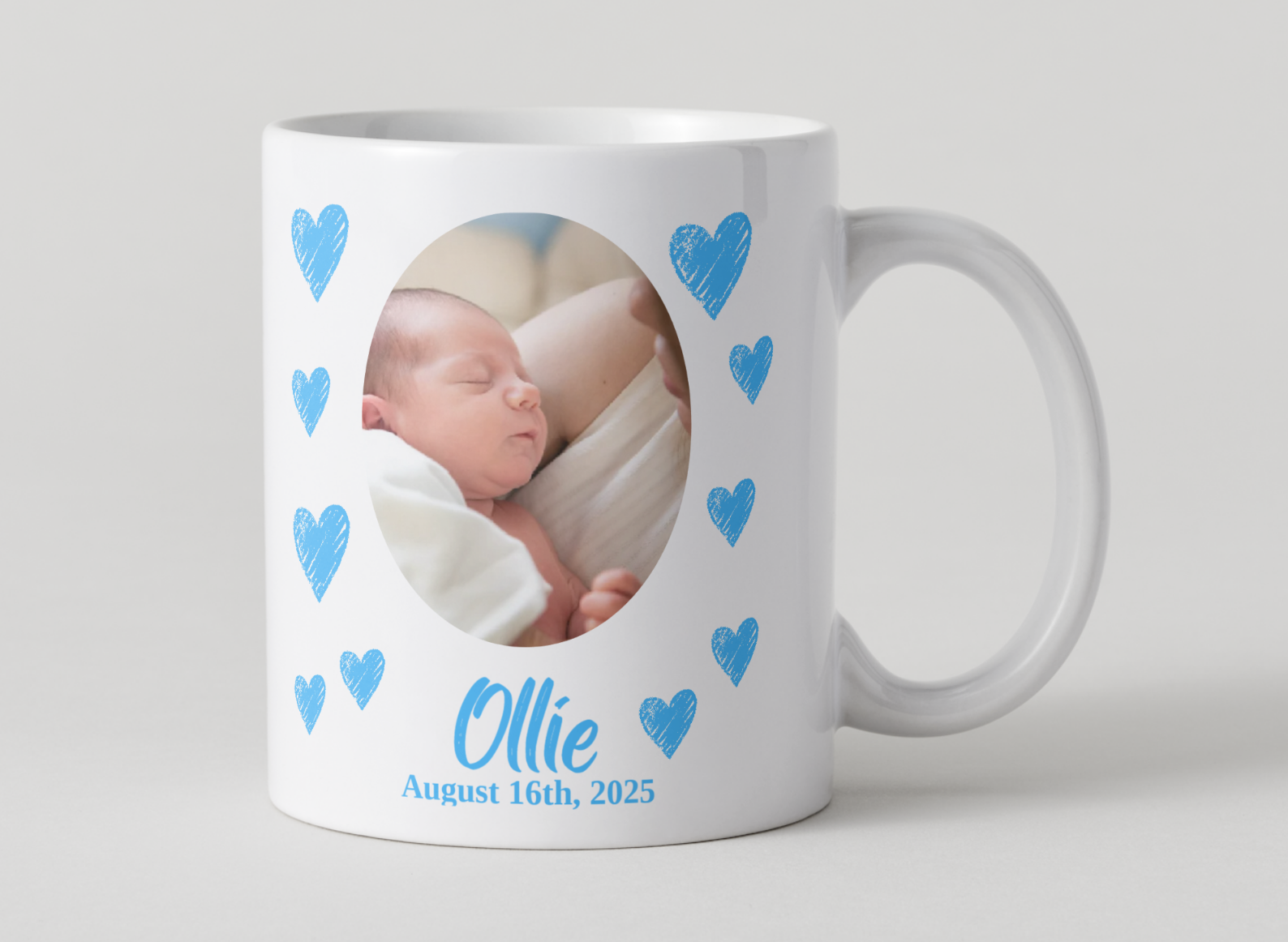 White mug with a photo of a baby and blue hearts, featuring the name 'Ollie' and date 'August 16th, 2025'.