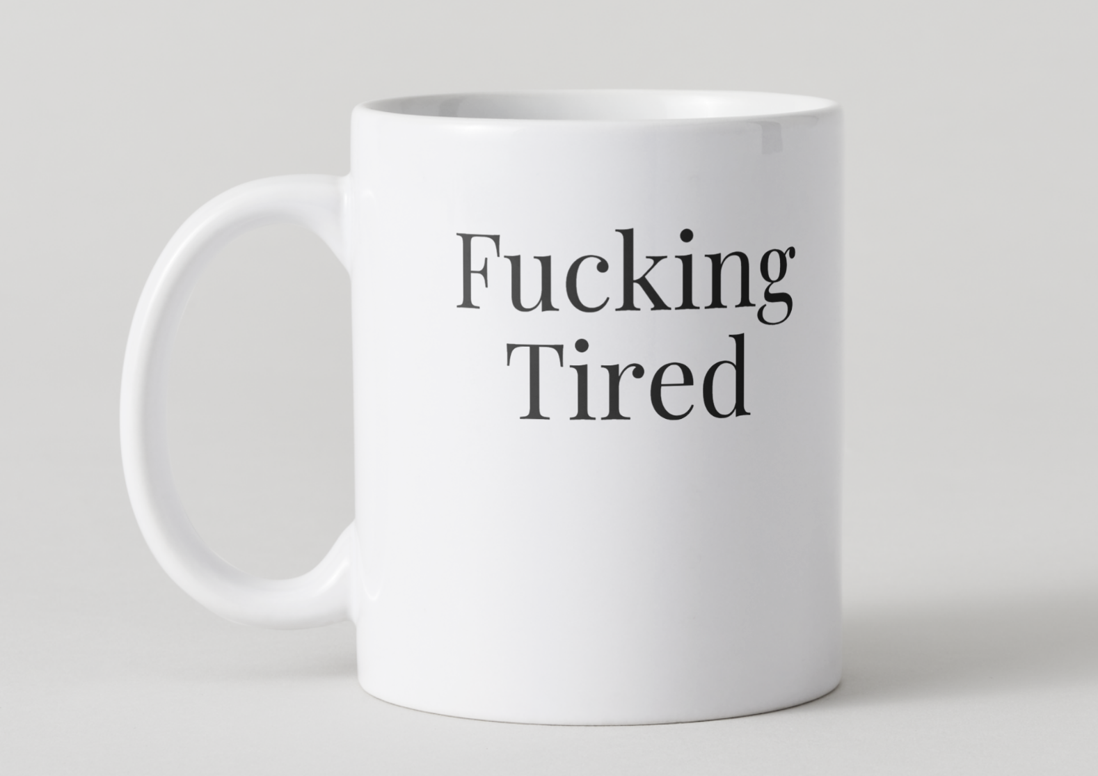 White mug with 'Fucking Tired' text on a light gray background