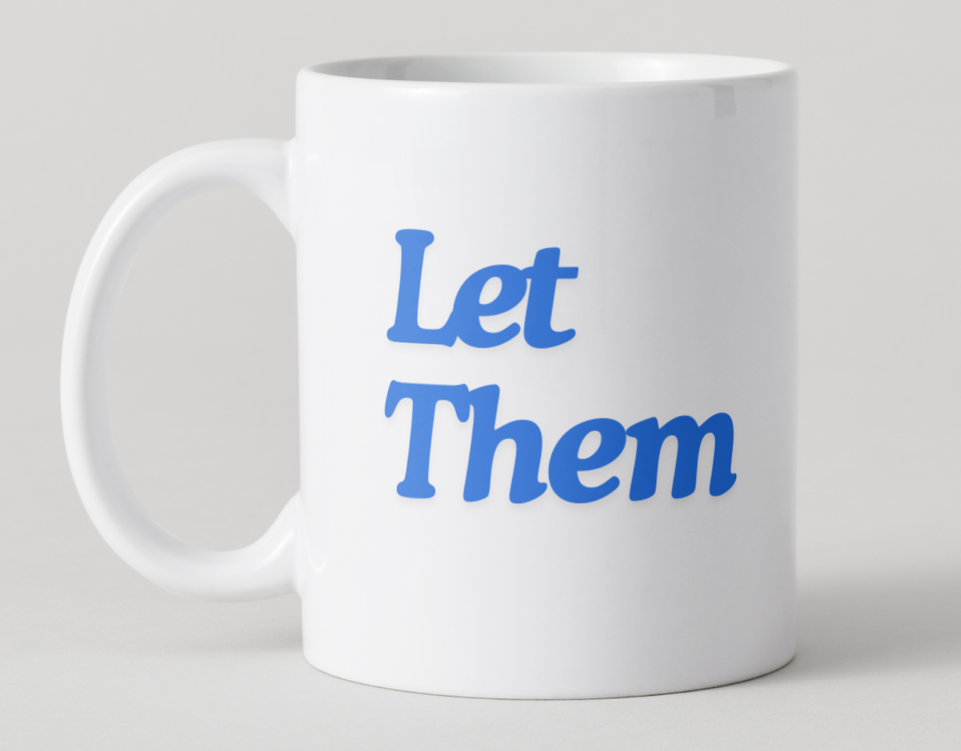 White mug with blue text 'Let Them' on a light gray background