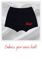 Black shorts with 'Slut!' text on a white background with red text below.