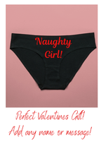 Black underwear with 'Naughty Girl!' text on a pink background