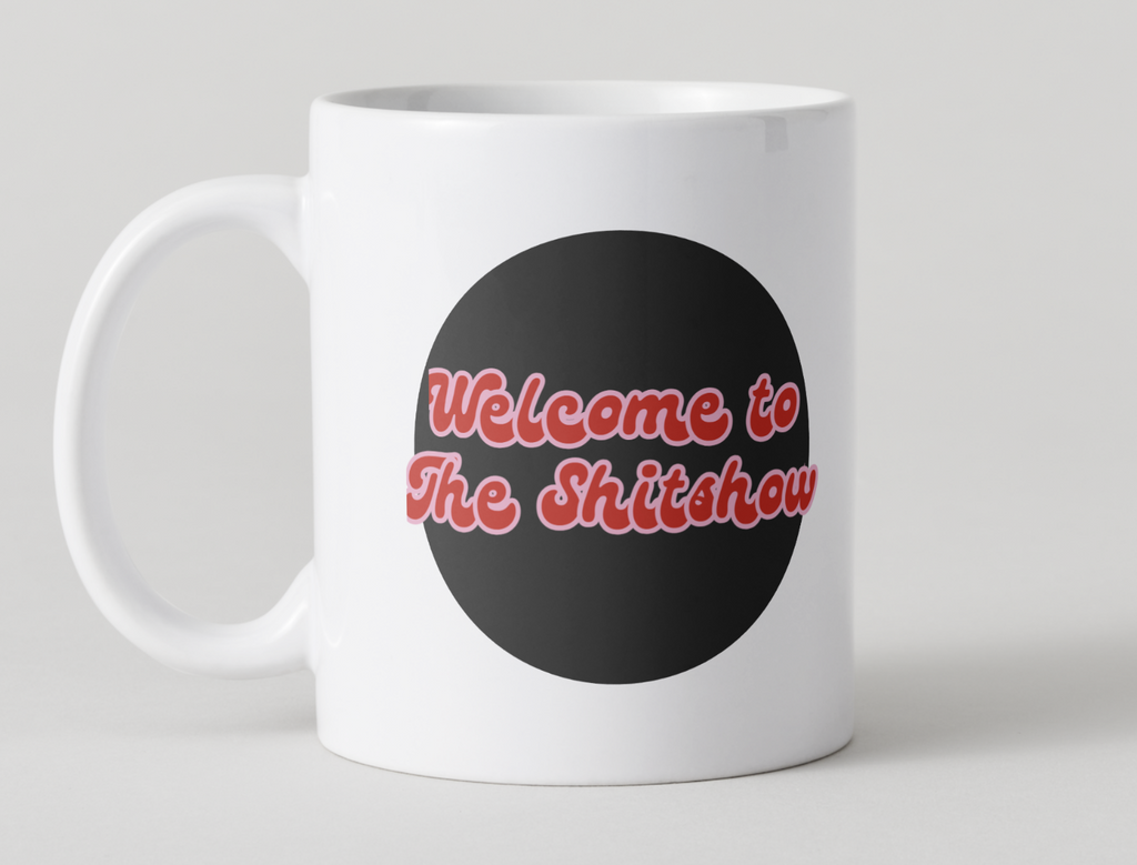 White mug with a black circle and red text "Welcome to the shitshow" on a light gray background