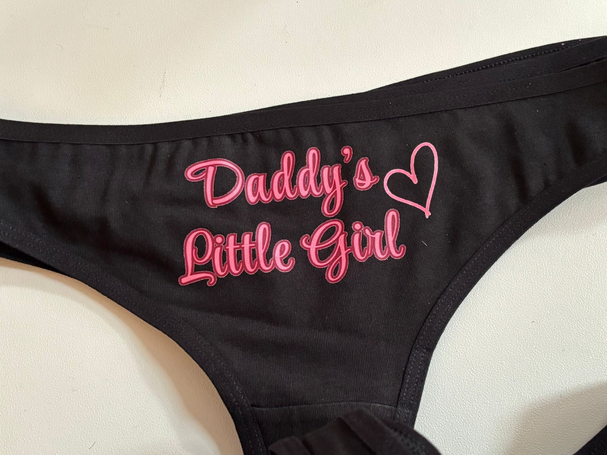 Black bralette with pink embroidered text reading 'Daddy's Little Girl' and a heart outline on the front, shown on a light background.