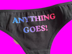 Black bikini bottoms featuring the phrase 'ANYTHING GOES!' printed vertically in a gradient of blue, purple, and pink, shown on a light-colored background.
