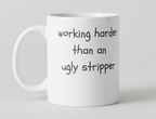 White mug with black 'Working harder than an ugly stripper' design on a light gray 