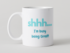 White mug with blue text 'shhh... I'm busy being tired!' on a light gray background