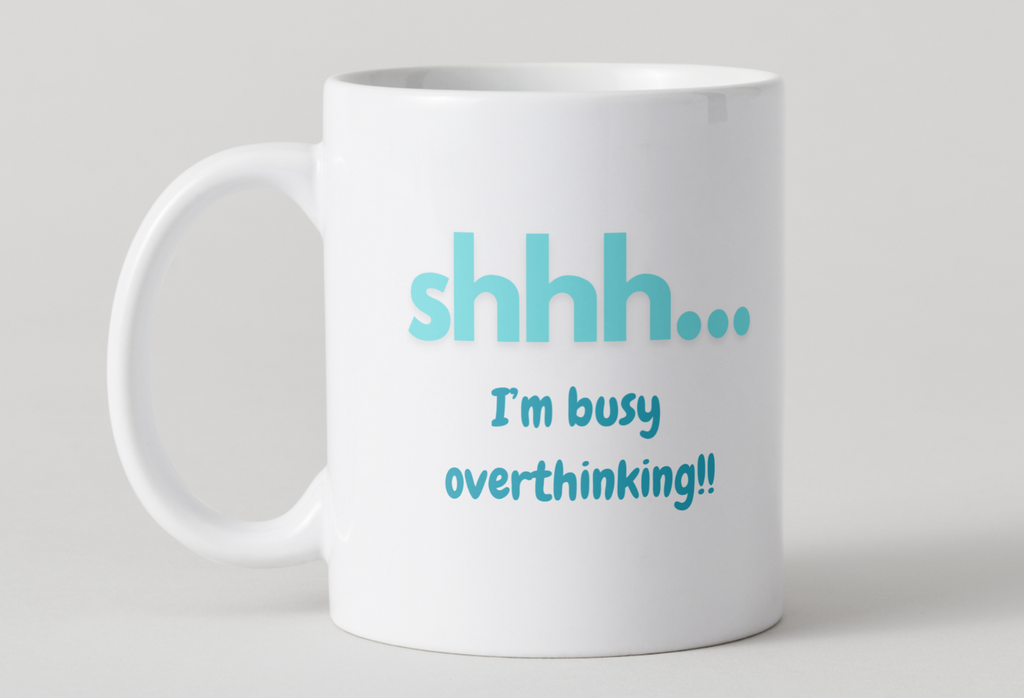 White mug with blue text 'shhh... I'm busy overthinking!' on a light gray background
