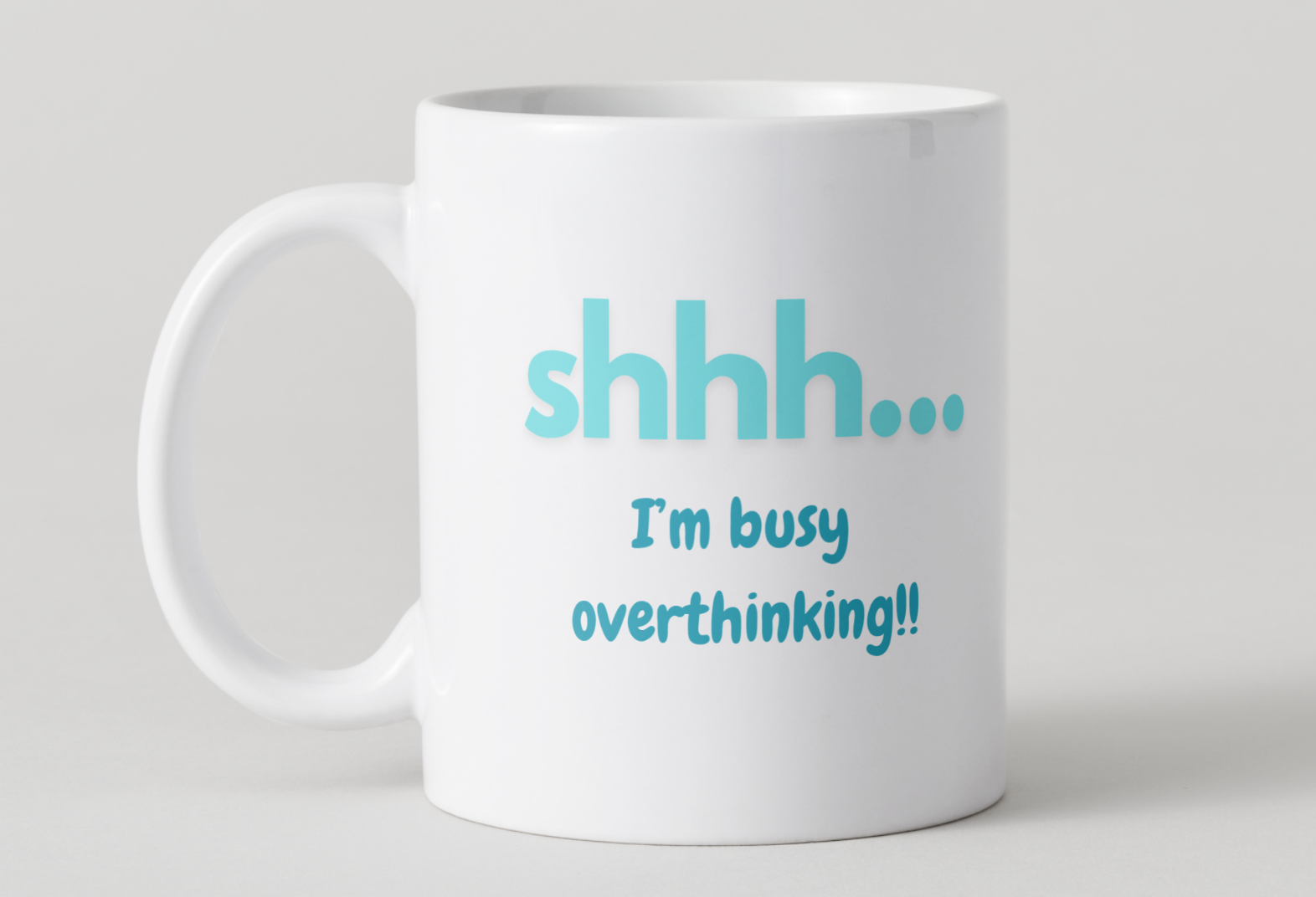 White mug with blue text 'shhh... I'm busy overthinking!' on a light gray background